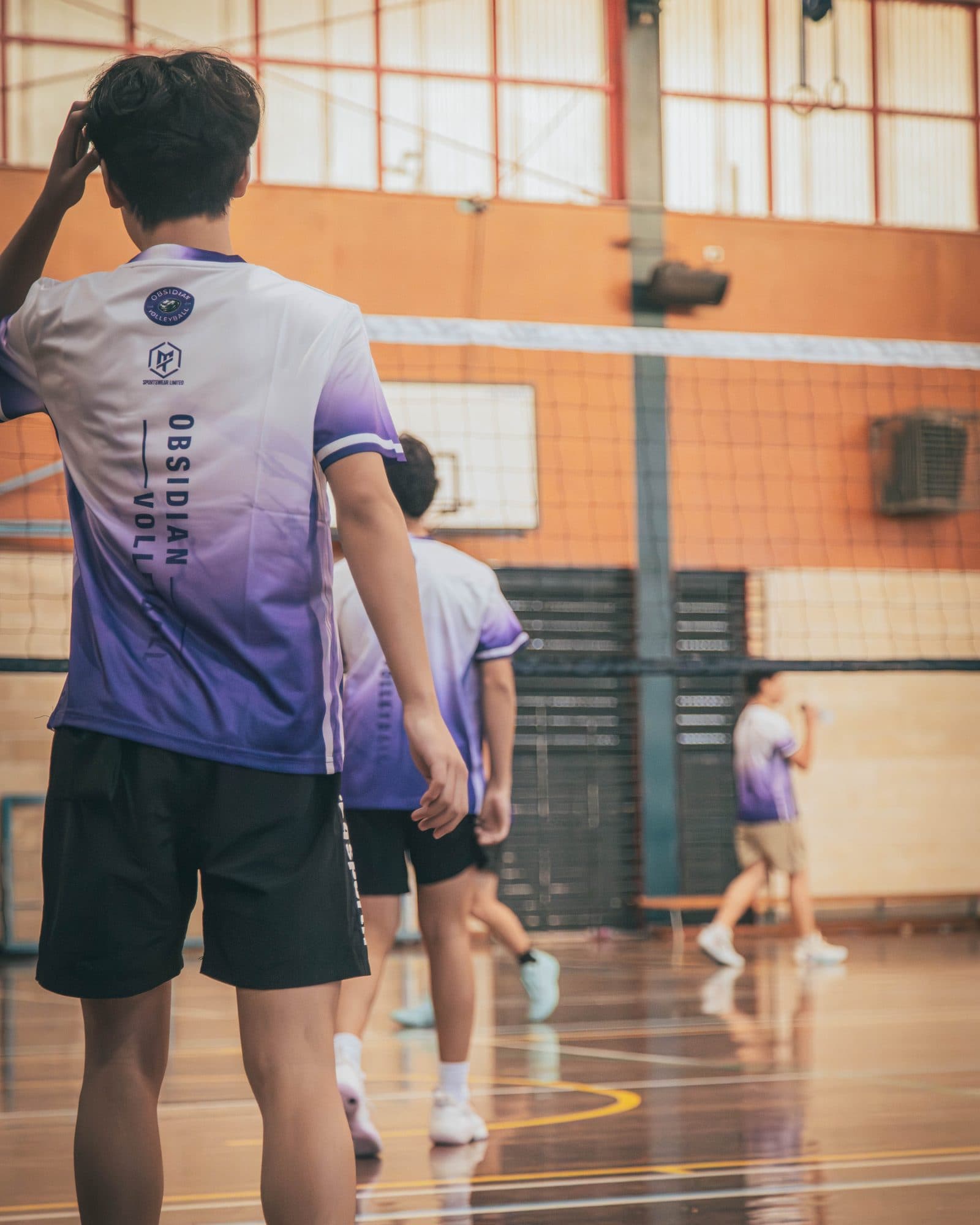 Junior player in an Obsidian jersey watching play from the back of the court