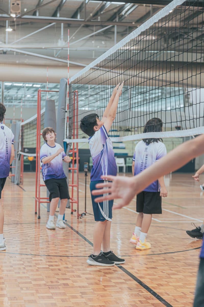 Junior player setting a volleyball while a coach shows a hand position in the foreground