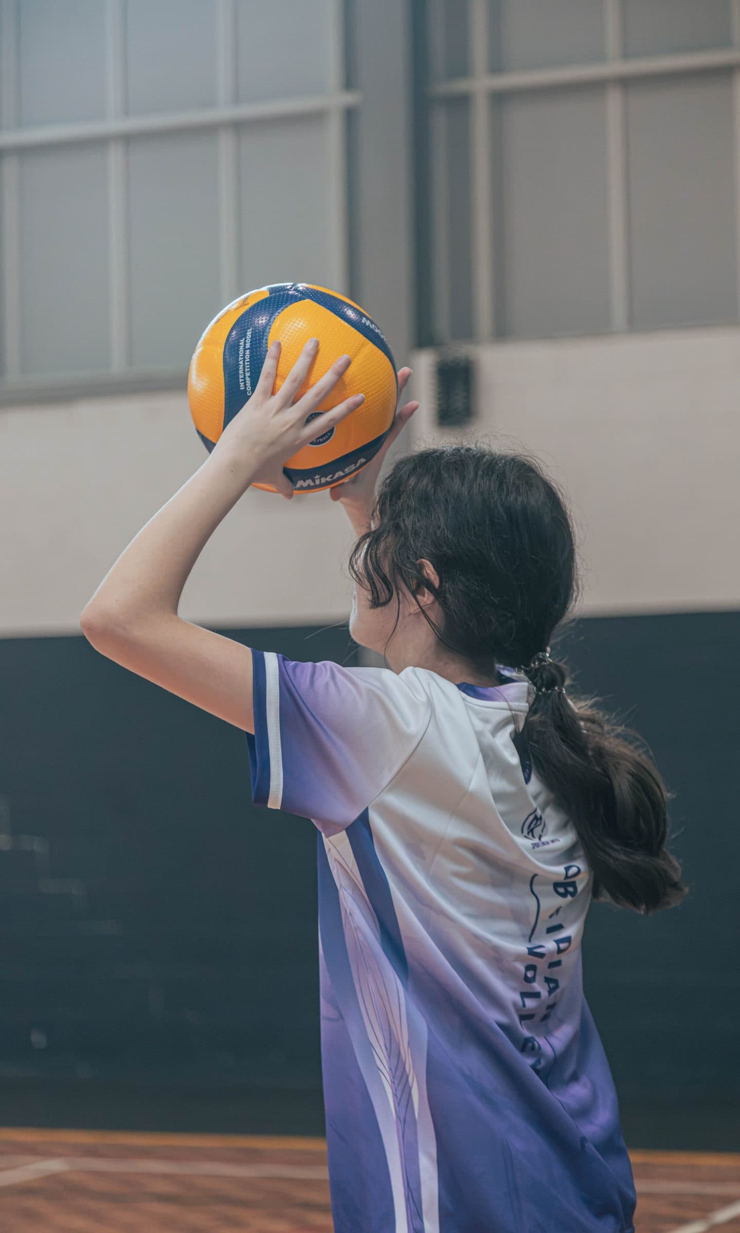 Girl in an Obsidian jersey holding a volleyball overhead, about to serve at Ryde Aquatic Leisure Centre