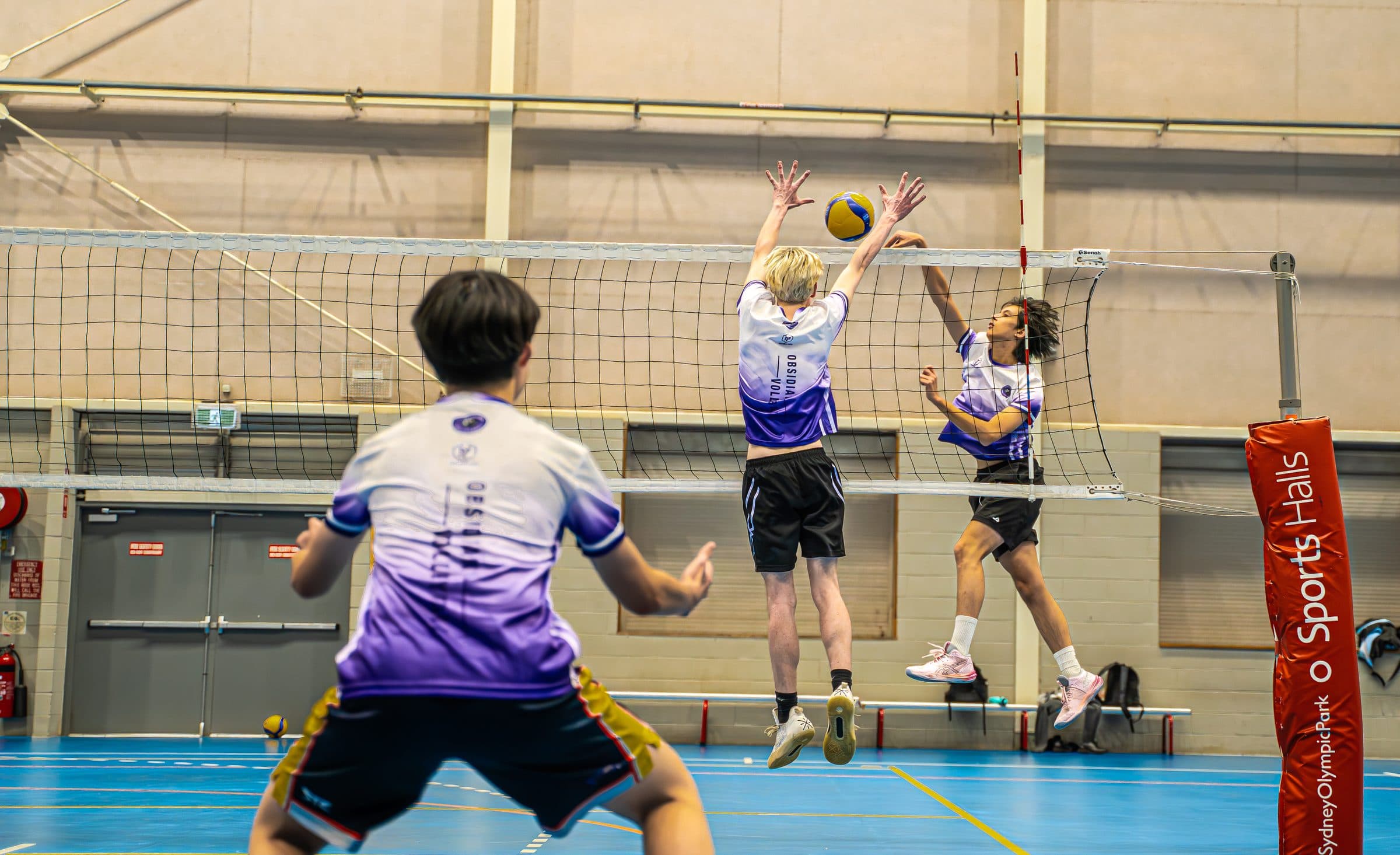 Two Obsidian players jump to block at the net on the blue courts at Sydney Olympic Park Sports Halls