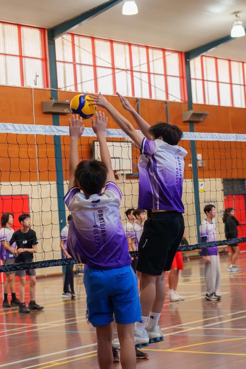 Three junior players jumping to block at the net during a game at Baulkham Hills